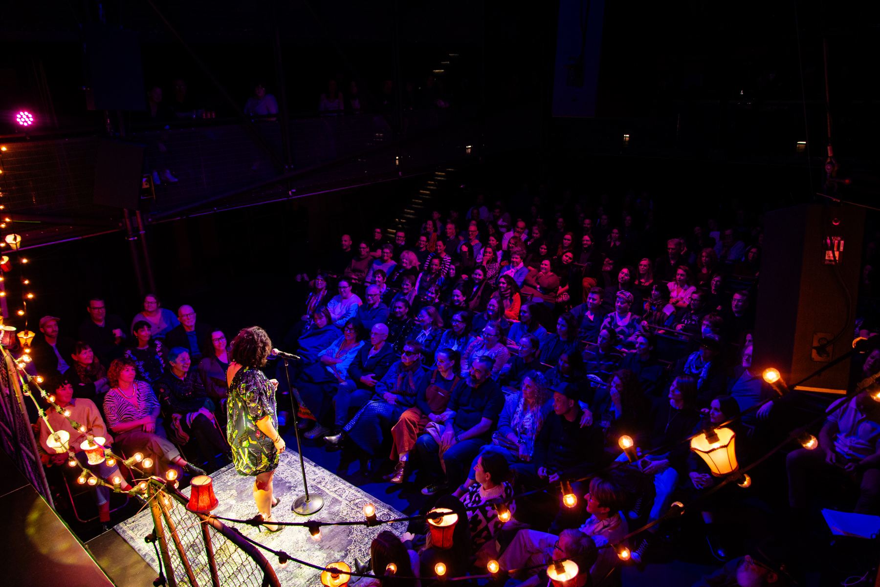 Victoria on stage at a microphone, speaking to a packed, smiling audience