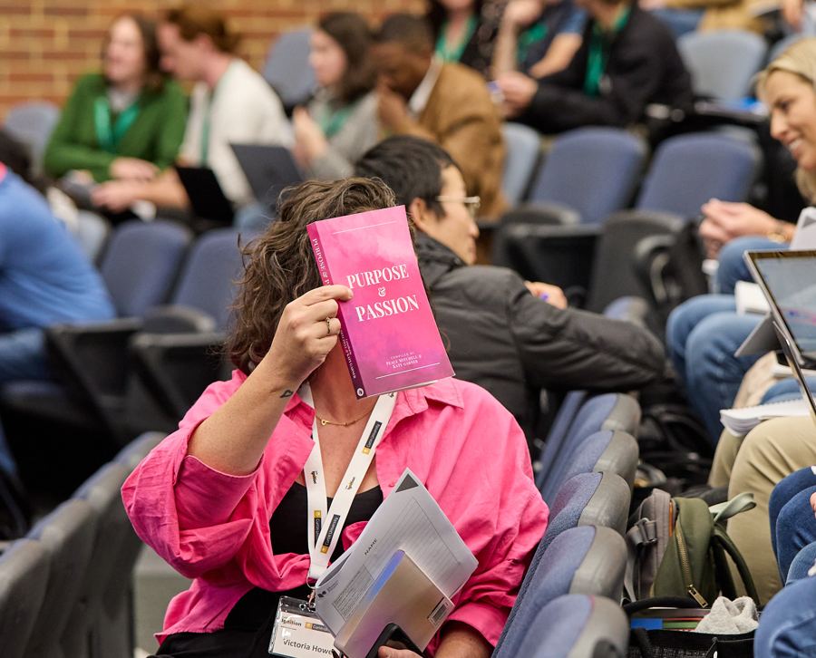 Victoria in a pink shirt holding up a copy of Purpose and Passion
